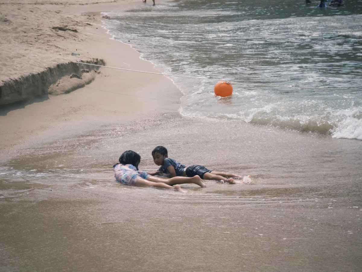 Lamma Island, Hong Kong — two kids lying in the shallow surf, an orange buoy floating behind them