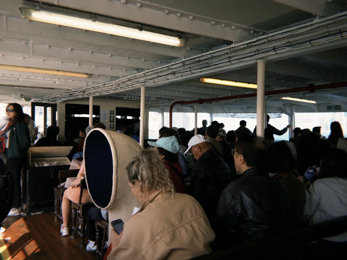 Inside a ferry cabin, passengers filling the benches, the far shore of the city through the window
