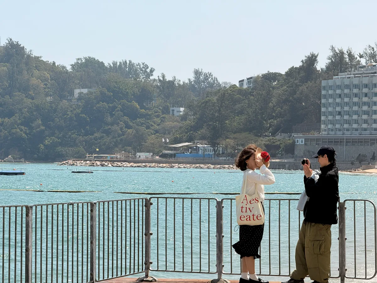 Cheung Chau, Hong Kong — at a railing by the sea, one person holding up a camera while another presses the shutter beside them